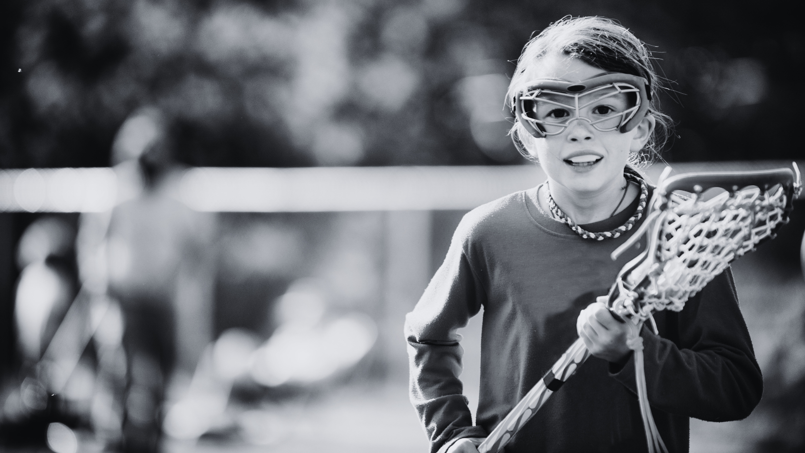 Black and white photo of a youth lacrosse player with a stick and goggles